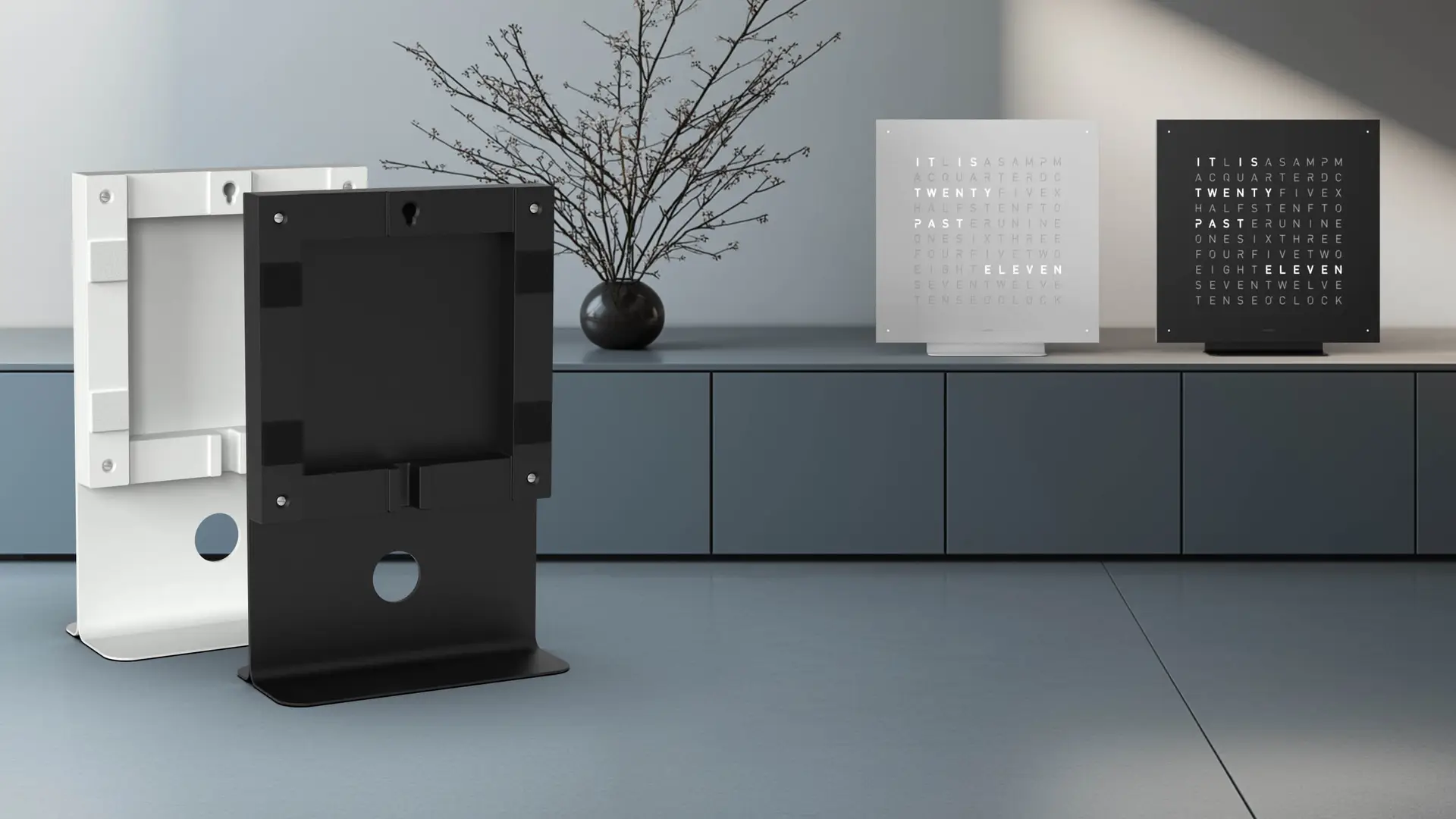 QLOCKTWO EARTH 45 in BLACK PEPPER und STAINLESS STEEL, Englisch, auf einem Sideboard mit passenden Ständern.